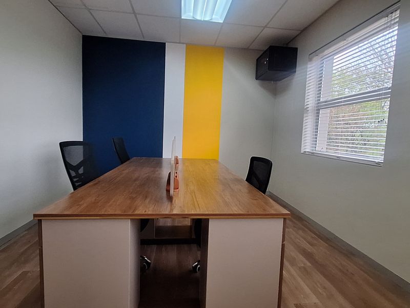 A functional office space featuring laminate flooring, a suspended ceiling, and a window with venetian blinds, accented by a feature wall.