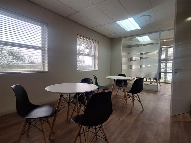 A bright office space featuring laminate flooring, a glass partition wall, and large windows with venetian blinds, providing a professional work environment.