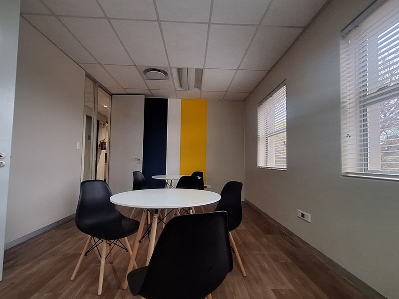 A bright, modern office space featuring laminate flooring, a suspended ceiling, and large windows with venetian blinds, providing a professional and functional work environment.