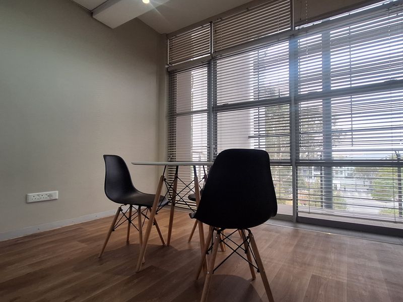 A bright office space featuring large floor-to-ceiling windows with venetian blinds and modern laminate wood flooring.