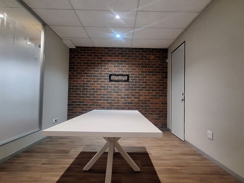 A modern office space featuring an exposed brick accent wall, glass partitioning, suspended ceiling, and durable laminate flooring.