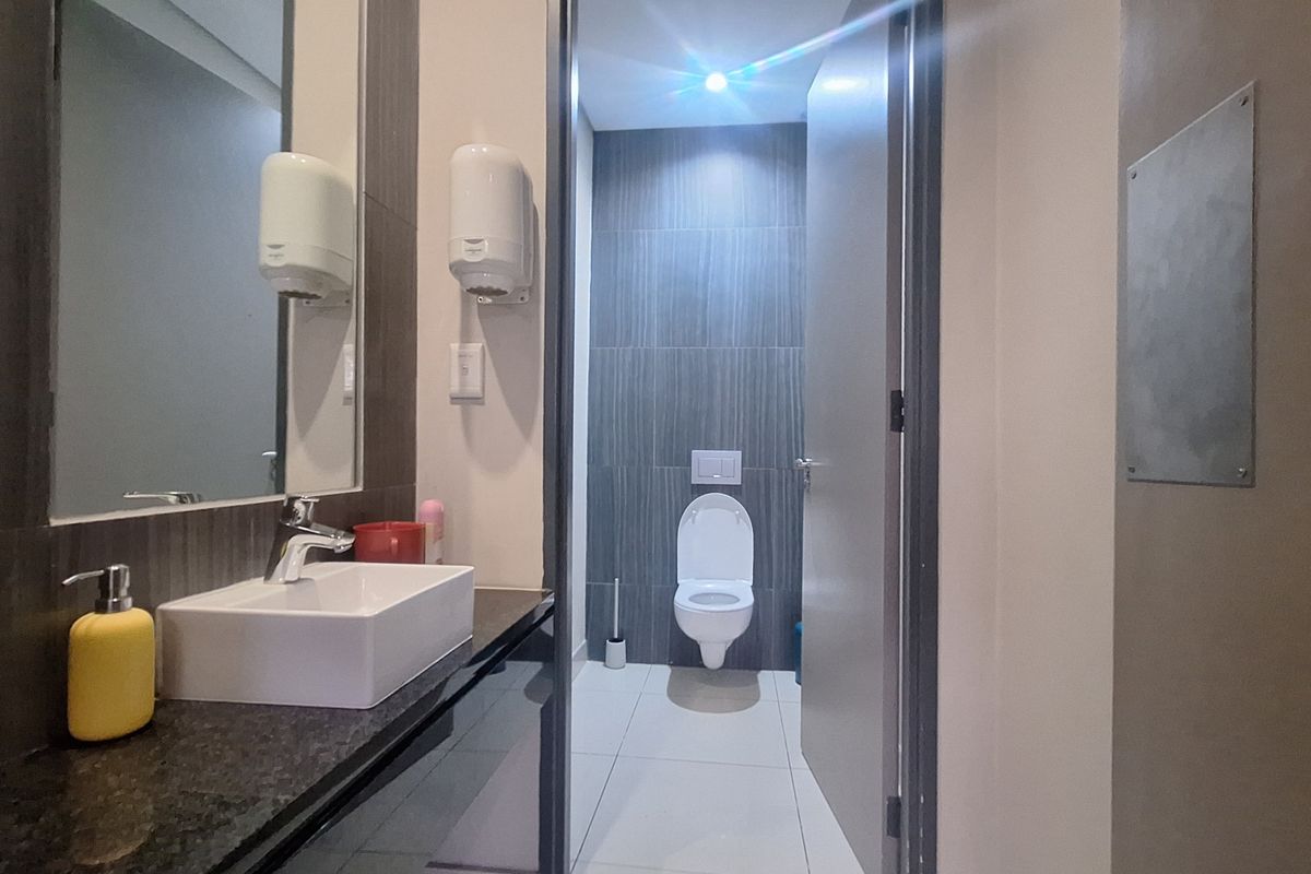 Modern office bathroom featuring a wall-mounted toilet, vanity basin with granite countertop, and contemporary tiled finishes.