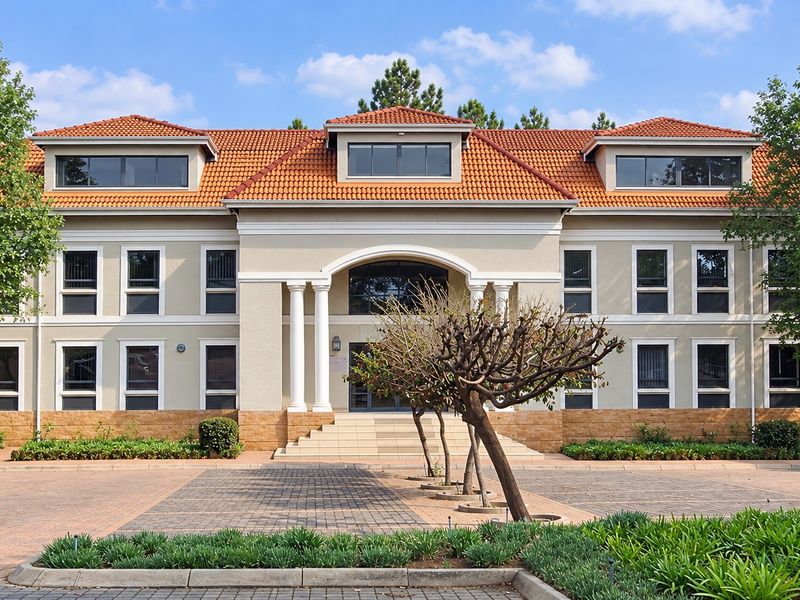 A well-maintained professional office building featuring a symmetrical facade, terracotta roof tiles, stone base detailing, and a grand columned entrance.