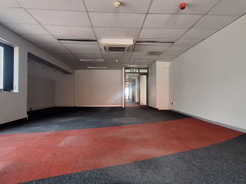 An empty, open-plan office space featuring a suspended ceiling with recessed lighting, integrated air conditioning, and multi-toned carpet flooring.