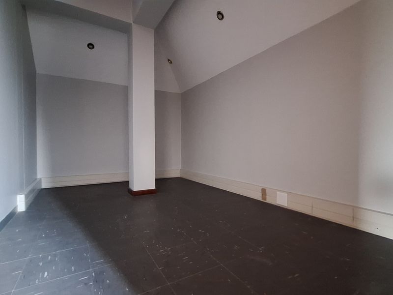 An empty office space featuring a central structural column, recessed downlighting, and dark tiled flooring with neutral wall finishes.