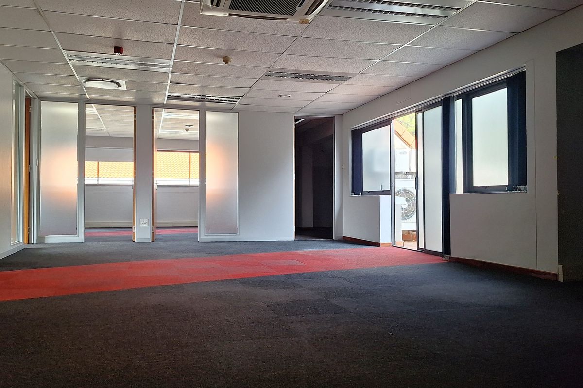 An empty open-plan office space featuring suspended ceilings, glass partitions, and carpeted flooring with access to an outdoor area.