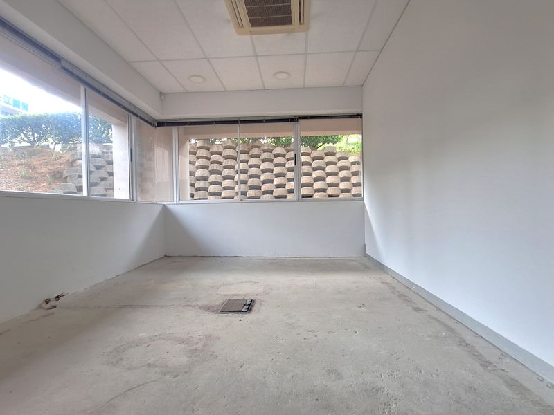 An empty office space featuring large windows, a suspended ceiling with recessed lighting, ducted air conditioning, and an unfinished concrete floor.