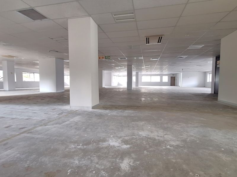 A large, open-plan office space featuring a suspended ceiling, recessed lighting, air conditioning units, and unfinished concrete flooring, ready for custom fit-out.