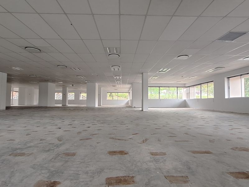 A large, open-plan office space featuring a suspended ceiling, recessed lighting, and expansive windows, currently awaiting final flooring installation.