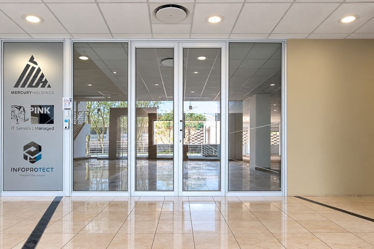 Professional office entrance featuring glass double doors, polished tile flooring, and a clean, modern reception area with corporate branding on the glass partition.