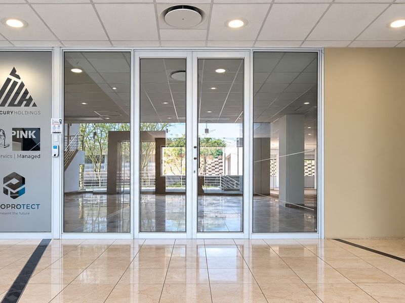 Professional office entrance featuring glass double doors, polished tile flooring, and a clean, modern reception area with corporate branding on the glass partition.