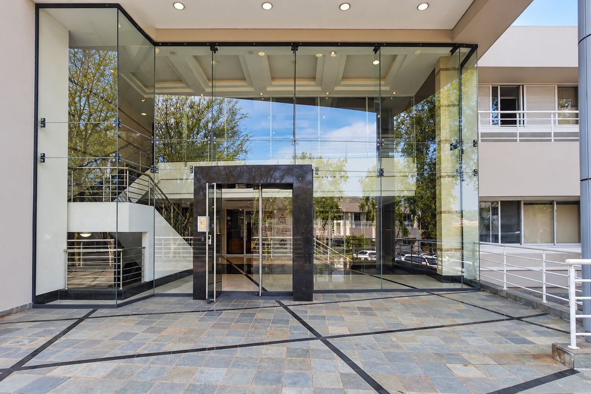 Modern office building entrance featuring a prominent glass facade, stone tile flooring, and a sleek stone-clad doorway.