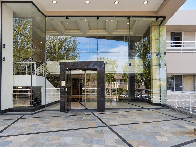 Modern office building entrance featuring a prominent glass facade, stone tile flooring, and a sleek stone-clad doorway.