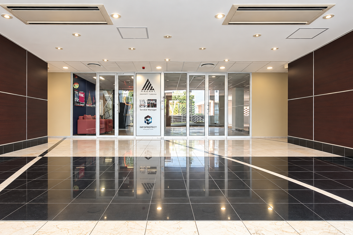 A professional office building entrance lobby featuring polished tiled flooring, dark wood wall paneling, and glass entry doors with integrated ceiling lighting.