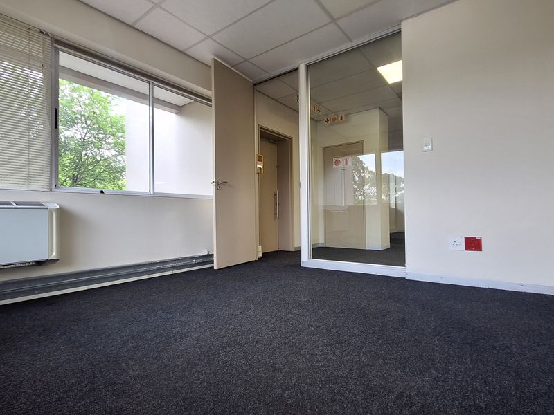 A vacant office space featuring a glass partition, suspended ceiling, carpeted flooring, and an integrated HVAC unit, offering a clean and functional workspace.