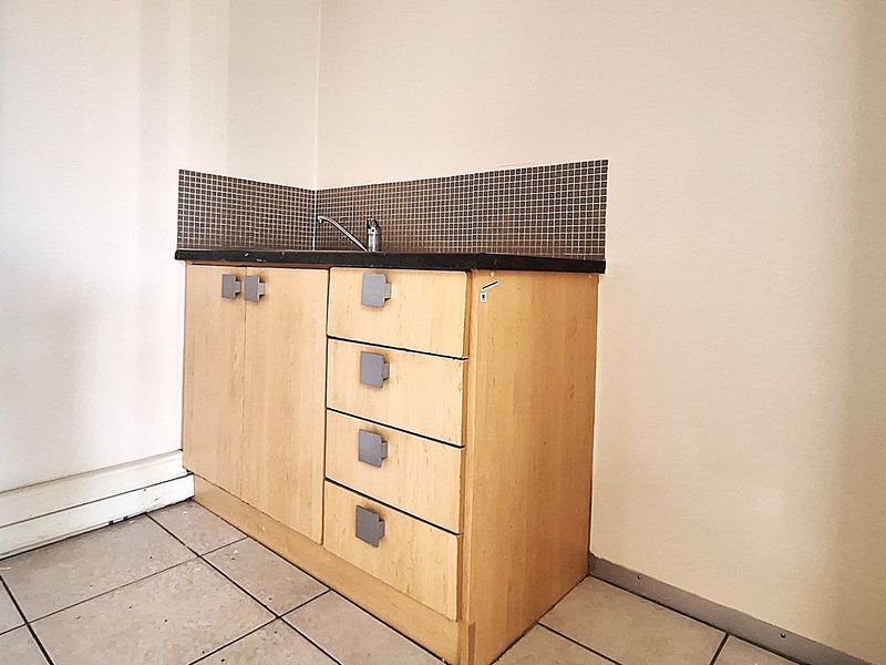 A compact kitchenette area featuring built-in wooden cabinetry, a sink with faucet, and a tiled backsplash, suitable for an office breakroom or utility space.