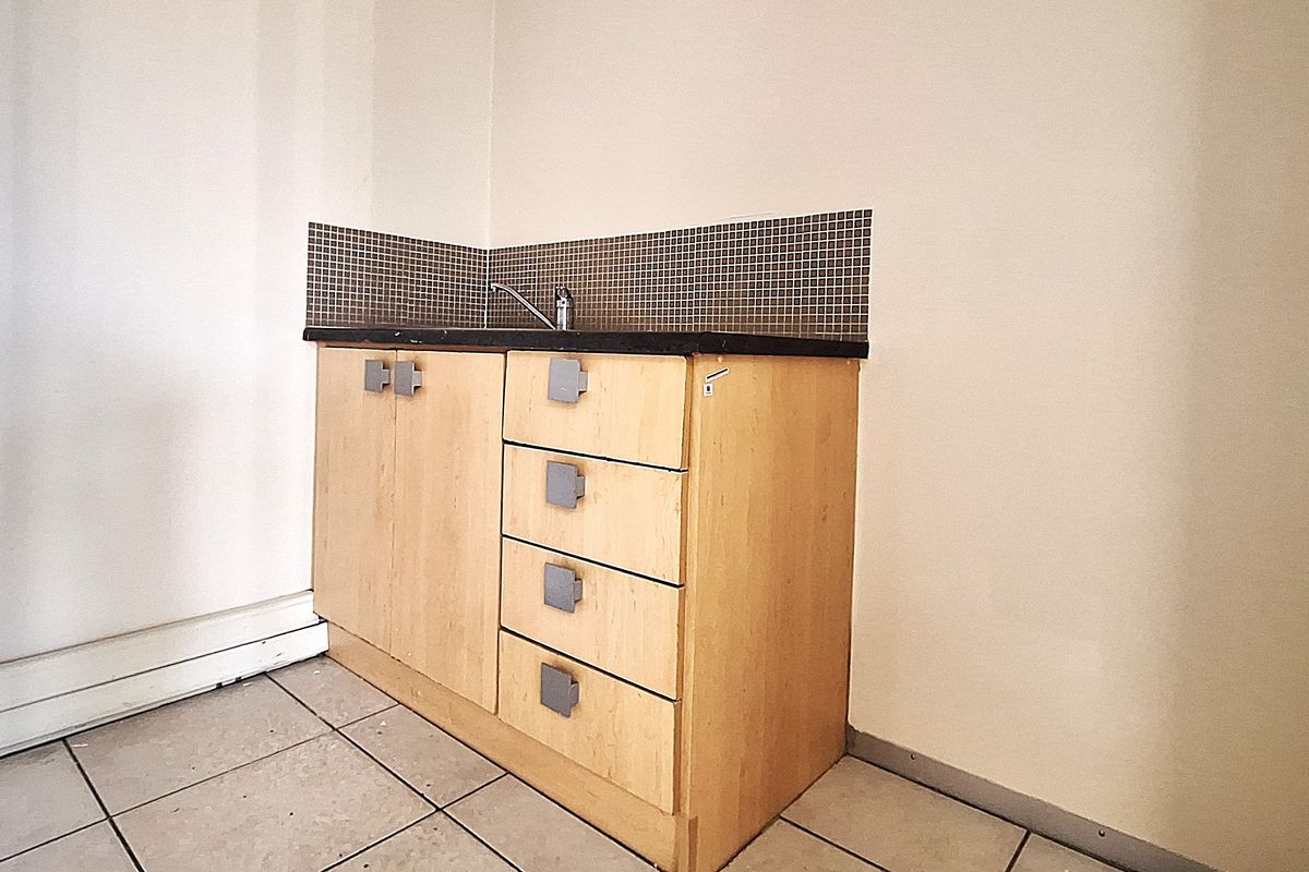 A compact kitchenette area featuring built-in wooden cabinetry, a sink with faucet, and a tiled backsplash, suitable for an office breakroom or utility space.