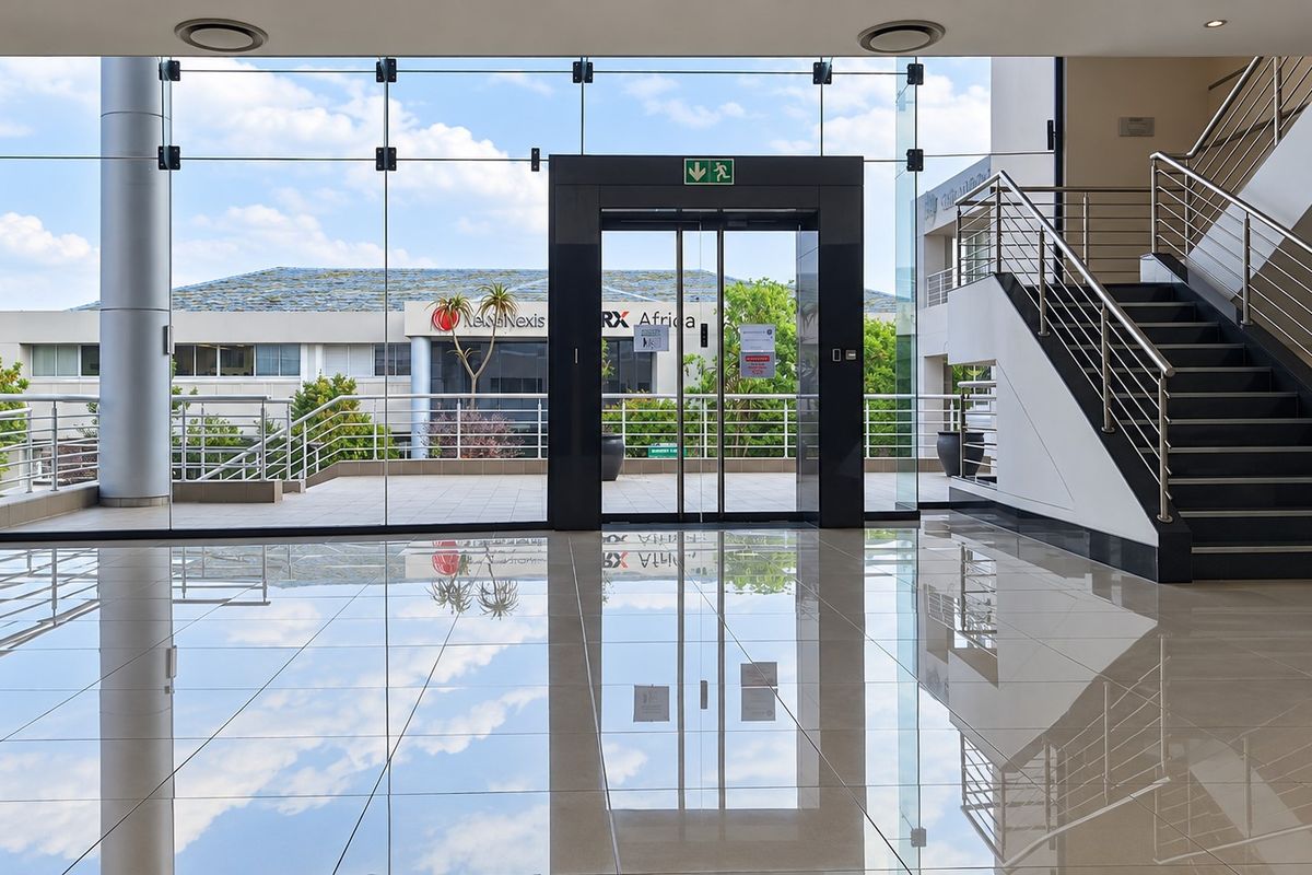 Modern office building entrance lobby featuring polished tile floors, a glass curtain wall, and a stainless steel staircase.