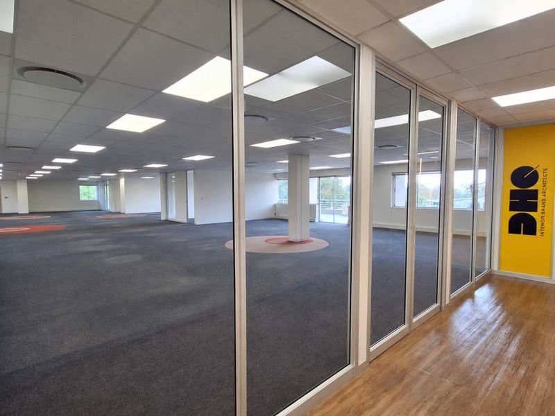 Spacious open-plan office area featuring glass partitions, suspended ceilings with recessed lighting, and a mix of carpet and laminate flooring.