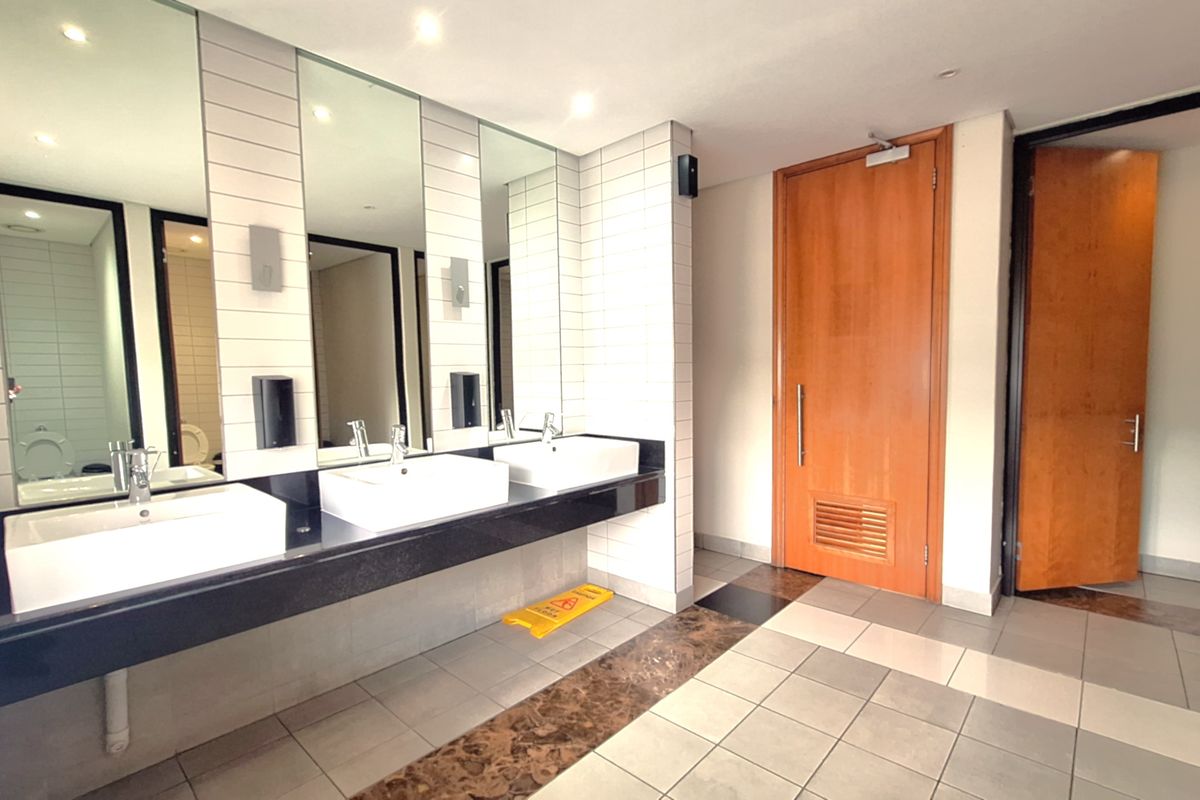 A clean, modern office bathroom featuring a triple vanity with vessel sinks, large mirrors, tiled backsplash, and durable ceramic flooring.