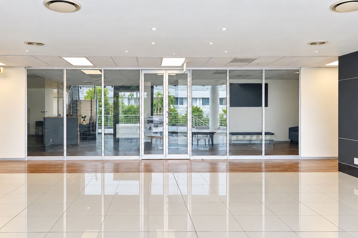 A bright, modern office reception area featuring polished tile flooring, glass partition walls, and a clean, professional aesthetic with recessed lighting.