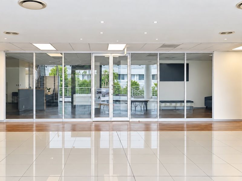 A bright, modern office reception area featuring polished tile flooring, glass partition walls, and a clean, professional aesthetic with recessed lighting.