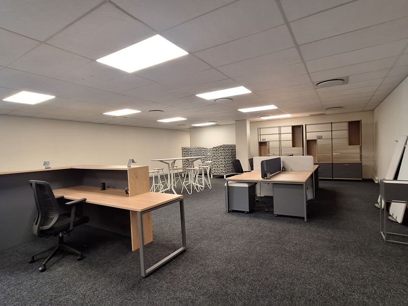 A spacious open-plan office area featuring suspended ceilings, recessed lighting, and durable carpet flooring, providing a functional and professional workspace environment.