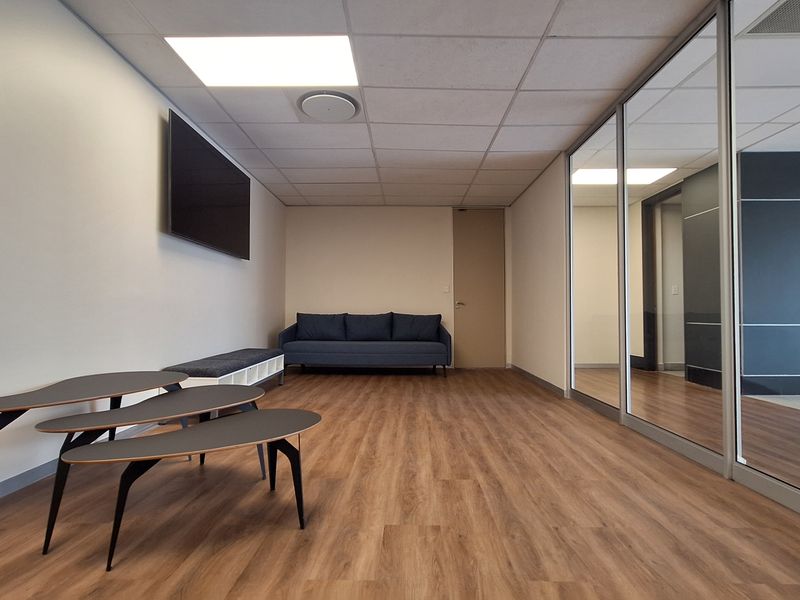 Modern office space featuring laminate flooring, a suspended ceiling with recessed lighting, and a glass partition wall providing a bright, professional work environment.