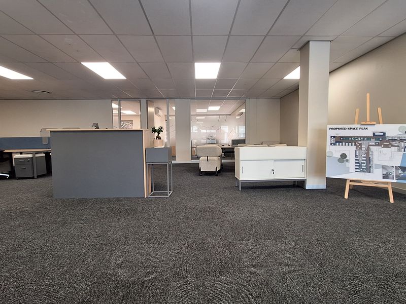 A professional open-plan office space featuring a suspended ceiling, recessed lighting, carpeted flooring, and glass partition walls for a modern, functional workspace.