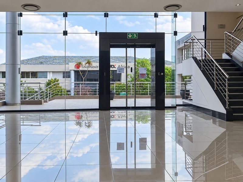 Modern office building entrance lobby featuring polished tile floors, a glass curtain wall, and a stainless steel staircase.