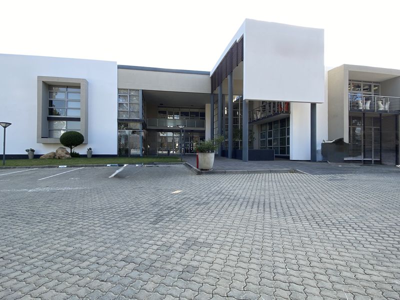 Modern office building exterior featuring a paved parking area, contemporary architectural facade, large glass windows, and a covered entrance.
