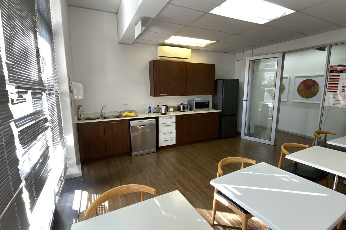 A functional office kitchenette featuring wood-finish cabinetry, laminate flooring, a stainless steel sink, and a glass partition door leading to an adjacent workspace.