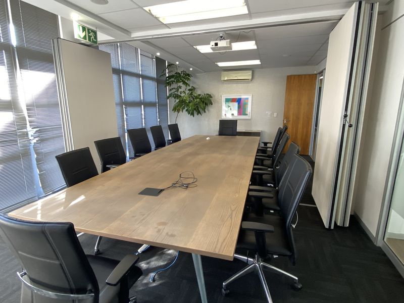 A professional office boardroom featuring a large meeting table, suspended ceiling with recessed lighting, air conditioning, and floor-to-ceiling windows with venetian blinds.
