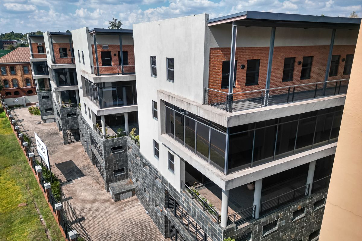 Aerial view of a modern multi-level office complex featuring brick and concrete facades, private balconies, and paved exterior parking areas.