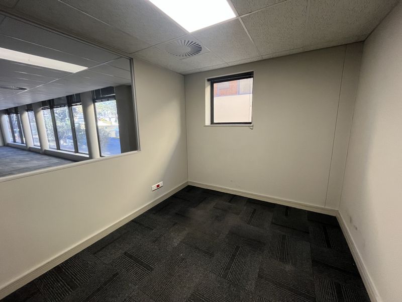 A vacant office space featuring carpet tiles, a suspended ceiling with recessed lighting, and an internal glass partition providing natural light.