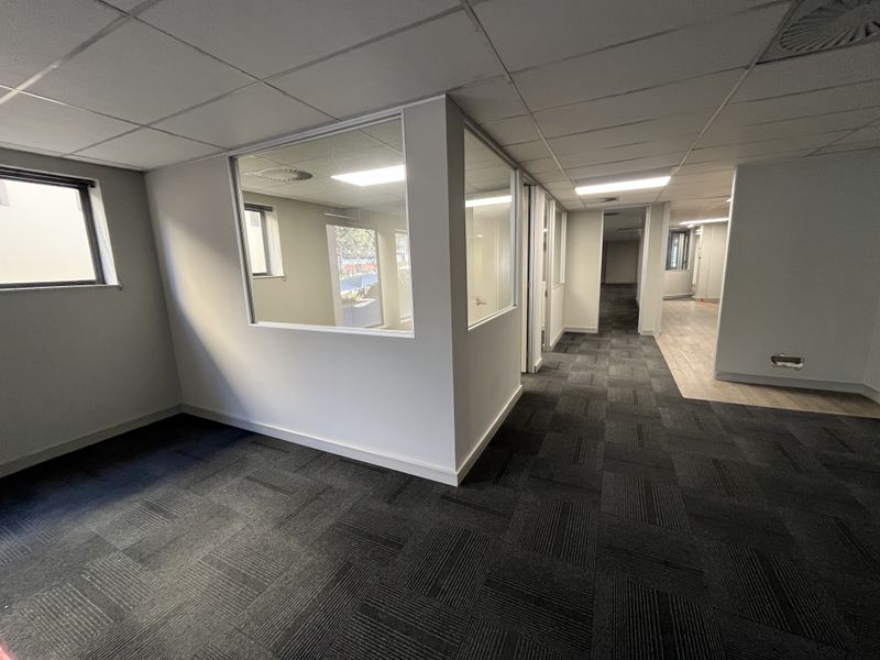 Modern vacant office space featuring glass partitions, suspended ceilings with recessed lighting, and a combination of carpet and laminate flooring.
