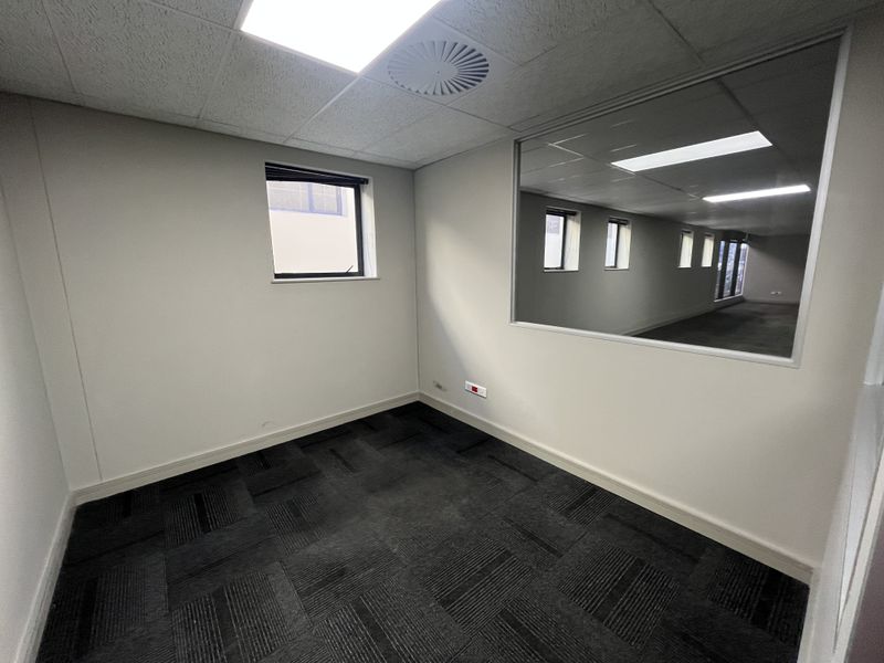 A clean, empty office space featuring carpet tiles, a suspended ceiling with recessed lighting, and an internal glass partition for natural light flow.