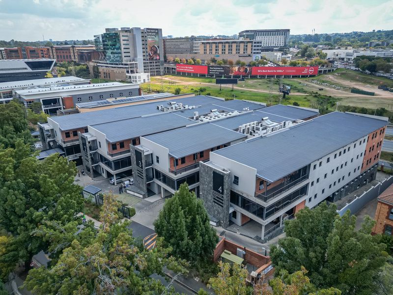 Aerial view of a modern multi-story office complex featuring metal roofing, integrated HVAC systems, and paved access areas within a landscaped business park setting.