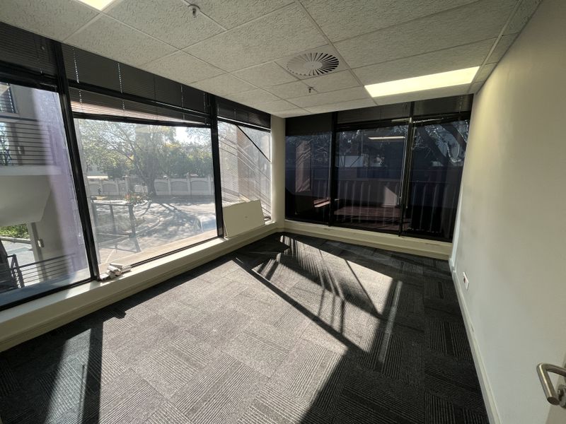 A bright, empty office space featuring large windows with venetian blinds, a suspended ceiling, and durable carpet tiles, suitable for a professional workspace.
