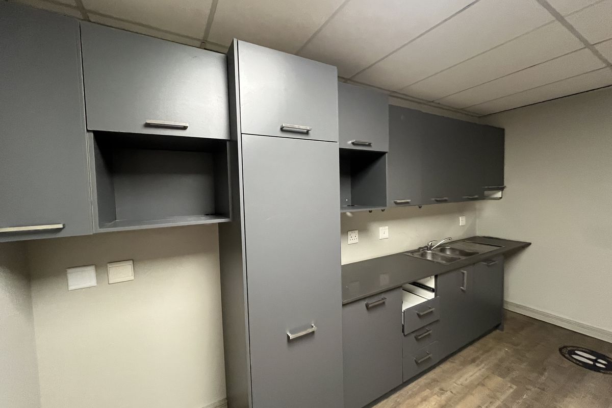 A functional office kitchenette featuring modern grey cabinetry, a stainless steel sink, and durable laminate flooring.