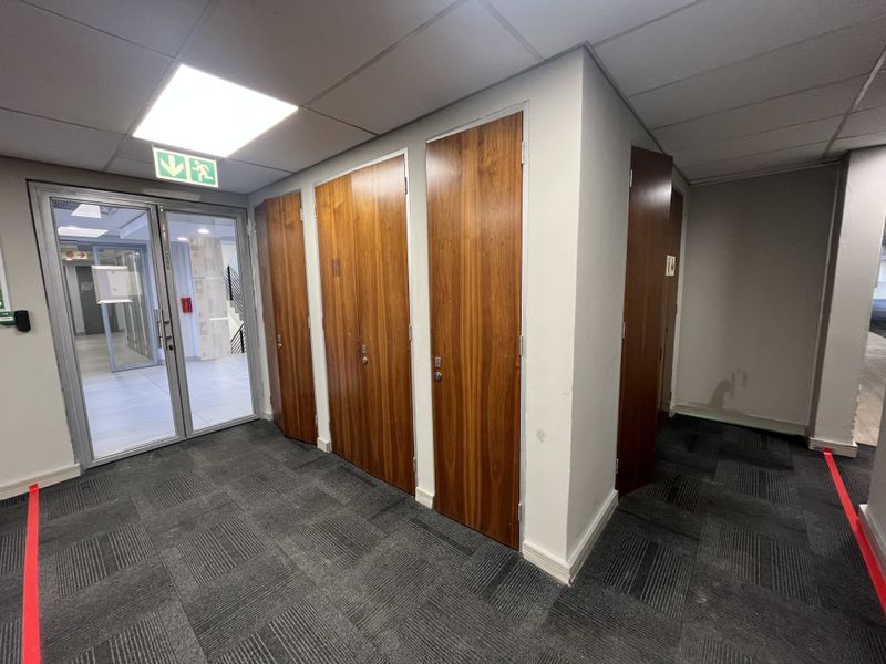 A functional office hallway featuring carpeted flooring, suspended ceiling with recessed lighting, and multiple wooden veneer doors leading to private office spaces.