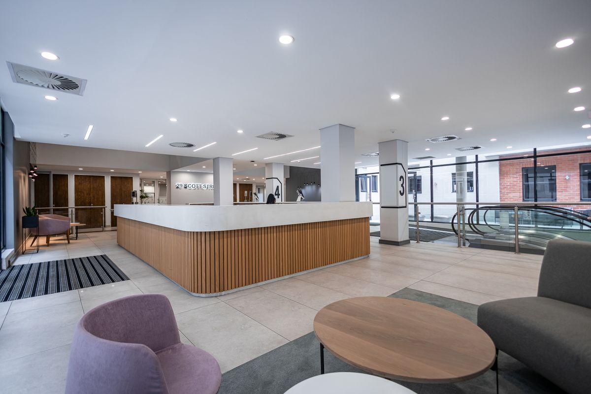 Modern office building lobby featuring a contemporary reception desk, tiled flooring, recessed lighting, and an escalator leading to other levels.