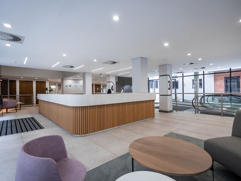 Modern office building lobby featuring a contemporary reception desk, tiled flooring, recessed lighting, and an escalator leading to other levels.