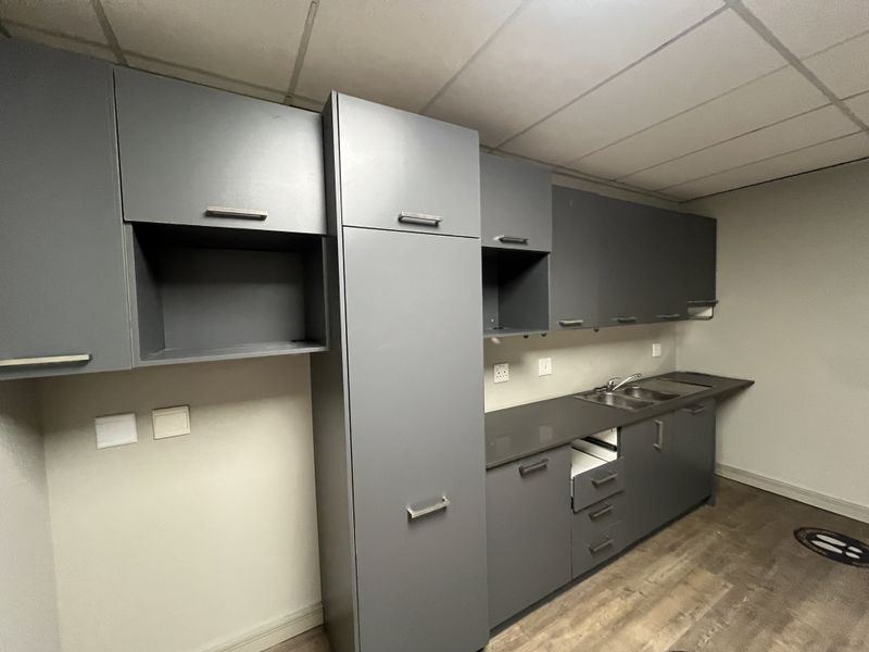A functional office kitchenette featuring modern grey cabinetry, a stainless steel sink, and durable laminate flooring.