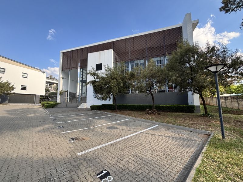 Modern office building exterior featuring a paved parking area, glass facade, and architectural louvre screening, presenting a professional and well-maintained corporate appearance.