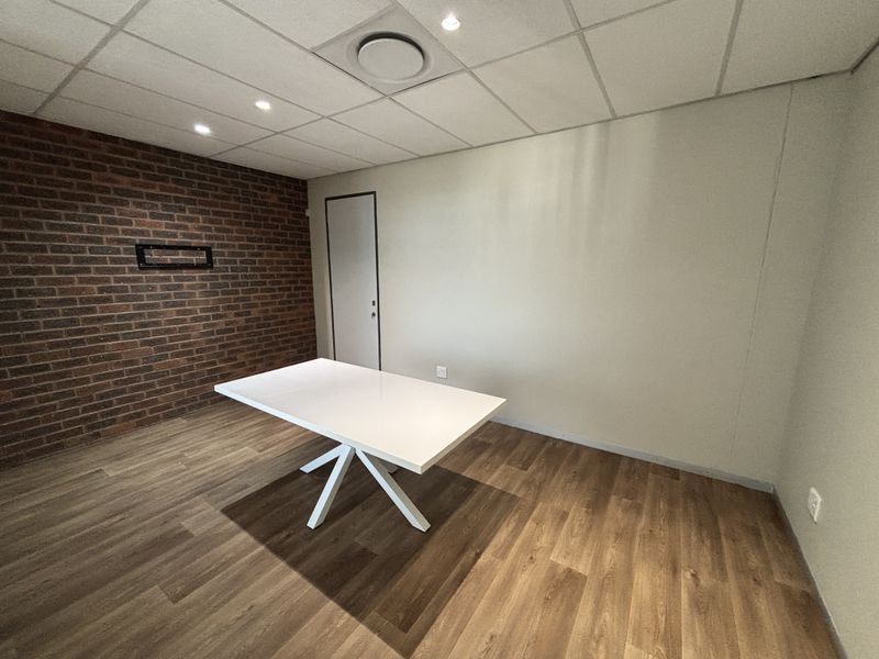 A clean, modern office space featuring an exposed brick accent wall, suspended ceiling with recessed lighting, and durable wood-look laminate flooring.
