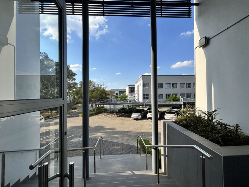 View from the office building entrance looking out over the paved parking area and surrounding office complex.
