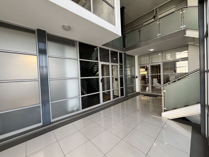 Modern office entrance foyer featuring high ceilings, polished tile flooring, and extensive glass partitioning with a mezzanine level and staircase.
