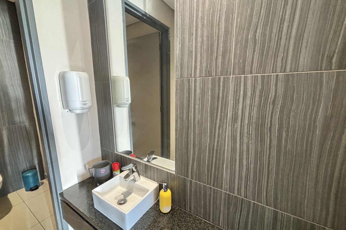 A modern office bathroom featuring a vessel sink, granite countertop, and contemporary grey wall tiling.