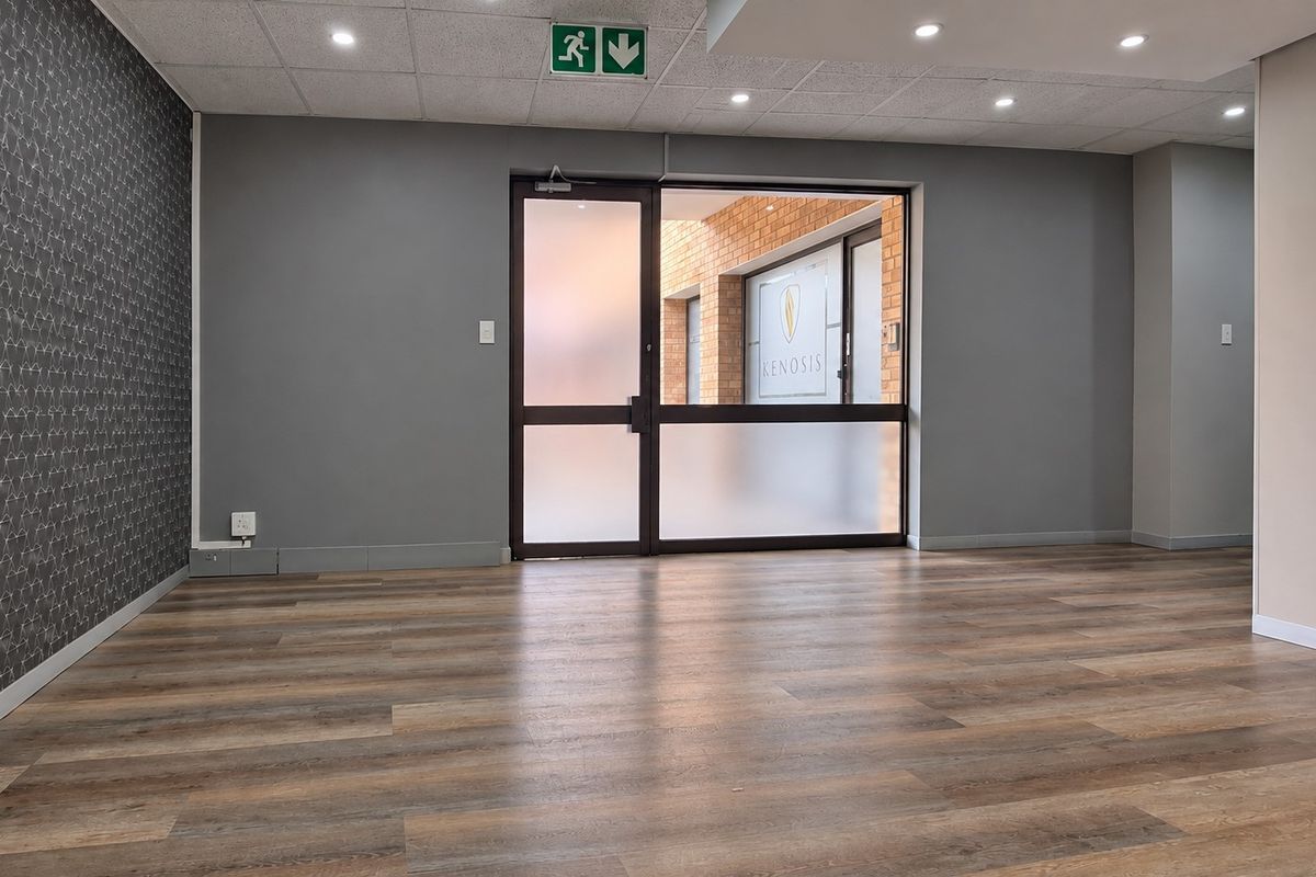 A bright, empty office space featuring modern laminate flooring, a suspended ceiling with recessed lighting, and a frosted glass entrance door.